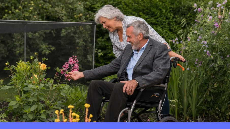 man in rolstoel met vrouw erachter in tuin