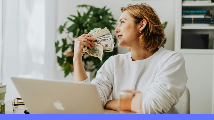 vrouw achter laptop met geld in haar hand.